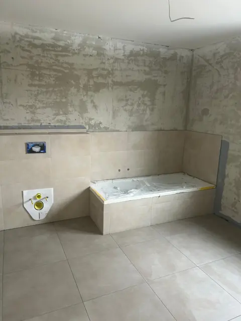 Bad mit Großformatfliesen, Badewanne und Vorwand im Rohbau